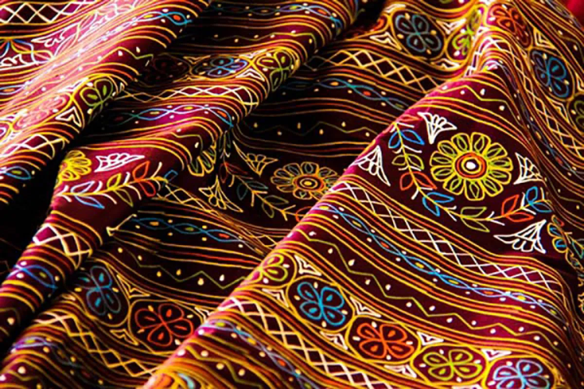 Artisan trailing Rogan paint from a metal rod onto cloth in Kutch